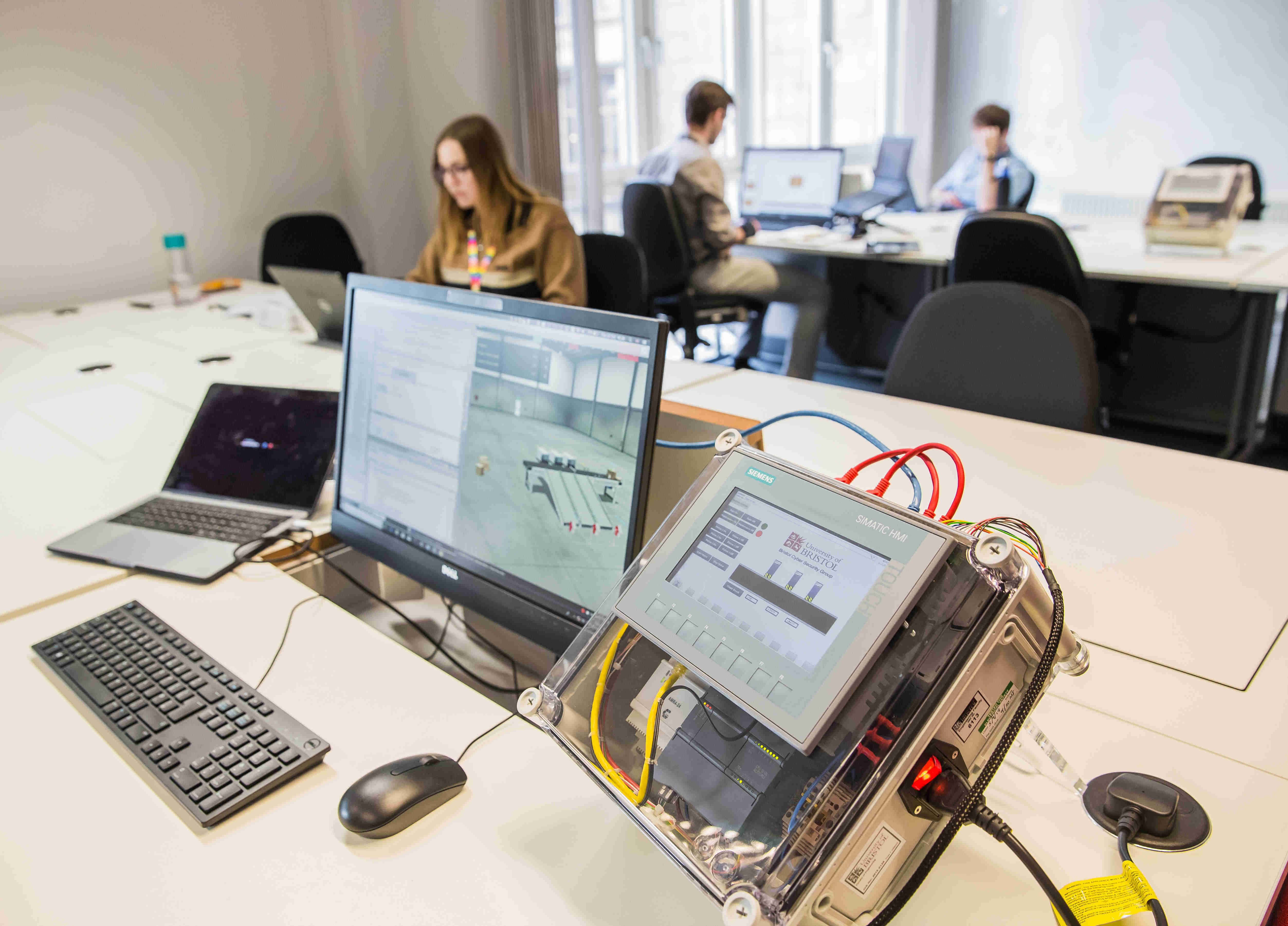 Students working in the background while a cyber security teaching box is in the foreground. 